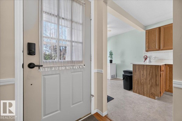 View of the entryway with a white door and a glimpse of the kitchen with light green walls. - 15228 84 St Nw, Edmonton