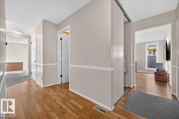 Hallway with wood laminate flooring, beige walls, and doorways leading to other rooms. - 15228 84 St Nw, Edmonton