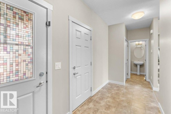 Interior entryway with beige tiled floor, white doors, and access to a powder room. - 1523 168 St Sw, Edmonton