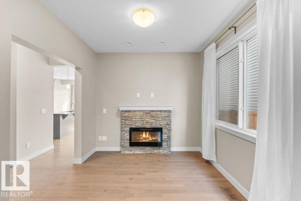 Living room with light wood floors, a stone-faced gas fireplace, and white curtains. - 1523 168 St Sw, Edmonton