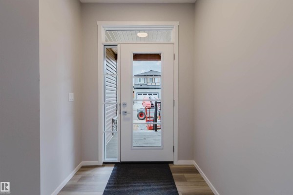 View through the front door shows a driveway with a red tractor and houses. - 1523 206 St Nw, Edmonton