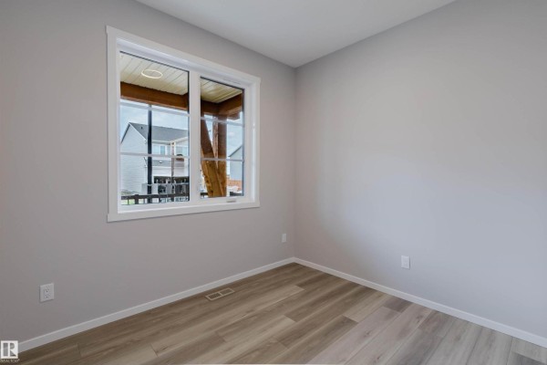 Empty room with light grey walls, a large window, and wood-look laminate flooring. - 1523 206 St Nw, Edmonton
