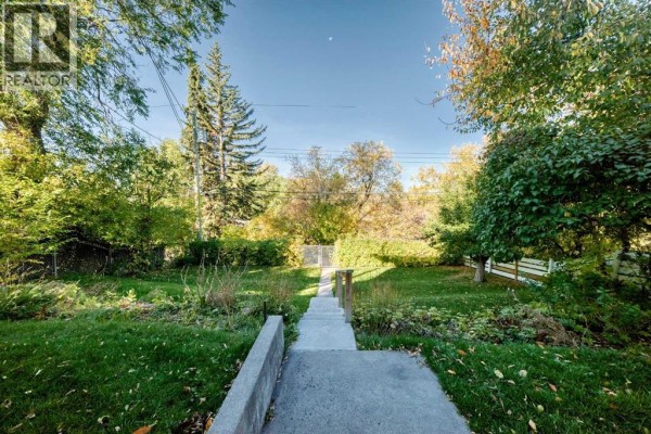 View of a backyard with green grass, trees, and a concrete pathway leading down. - 1523 23 Street Nw, Calgary