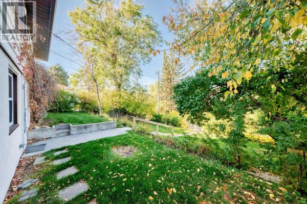 Side view of a house with a concrete patio, flagstone path, and lush green lawn. - 1523 23 Street Nw, Calgary