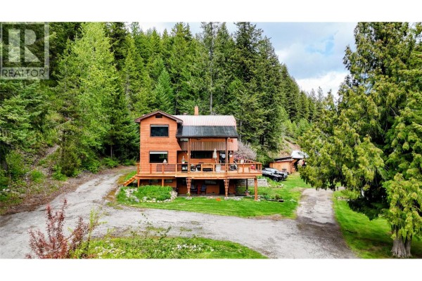 View of the wooden house and driveway from a distance, surrounded by trees. - 1525 Highway 3 / 95 Highway, Yahk