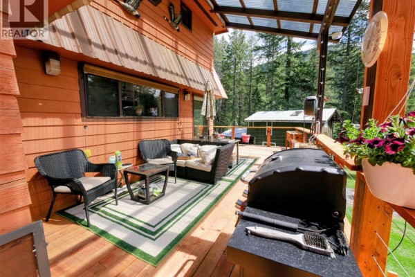 Covered outdoor deck area with wicker furniture, rug, and gas grill. - 1525 Highway 3 / 95 Highway, Yahk