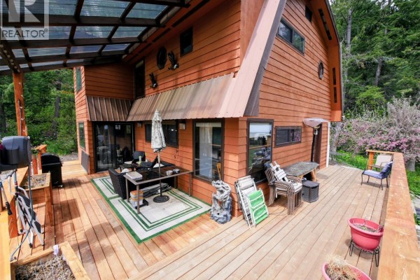 Spacious wooden deck with outdoor dining set, chairs, and grill, partially covered. - 1525 Highway 3 / 95 Highway, Yahk