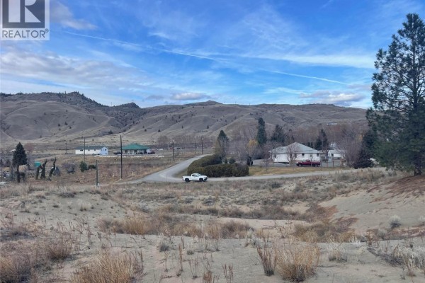 Road view with scattered homes and hills, featuring a white vehicle in the foreground. - 1525 Steelhead Road, Kamloops