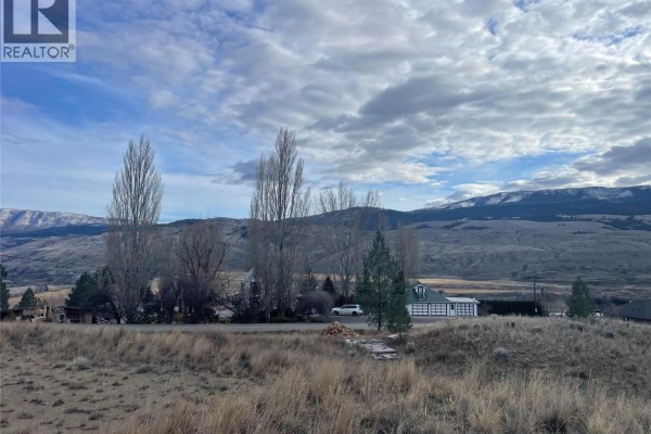 Landscape view of the property with distant homes and trees, against a backdrop of rolling hills. - 1525 Steelhead Road, Kamloops