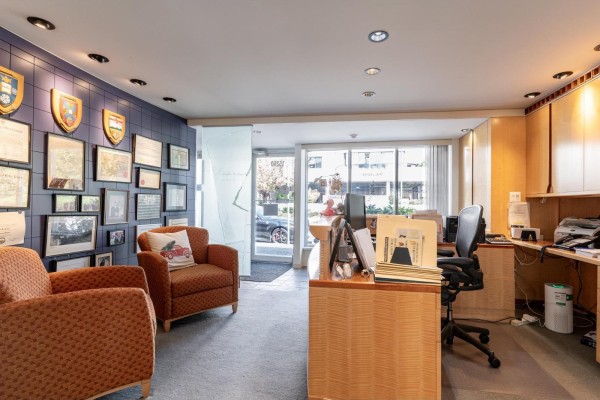 Office waiting area with two patterned chairs, reception desk, and framed documents on a blue tiled wall. - 15258-15260 Thrift Avenue, White Rock