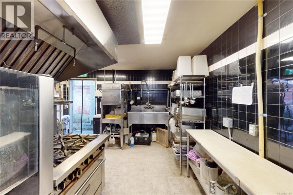 Commercial kitchen with stainless steel appliances, a large range hood, and black tiled walls. - 1527 Amelia St, Victoria