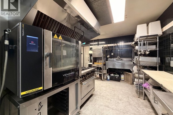 Commercial kitchen with a combi oven, gas range, stainless steel work surfaces, and black tiled walls. - 1527 Amelia St, Victoria
