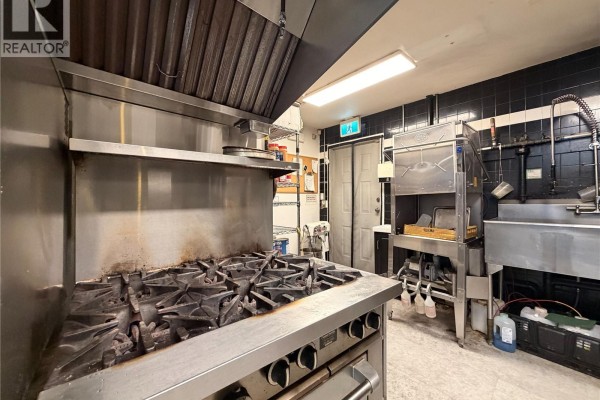 Close-up of a commercial gas range with a large stainless steel hood above it. - 1527 Amelia St, Victoria