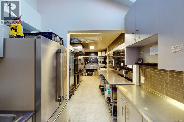 Long commercial kitchen with stainless steel refrigerators, ovens, a sink, and shelving on both sides. - 1527 Amelia St, Victoria