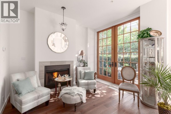 Living room with gas fireplace, two armchairs, ottoman, and glass doors to the garden. - 1527 Atlas Lane, Vancouver