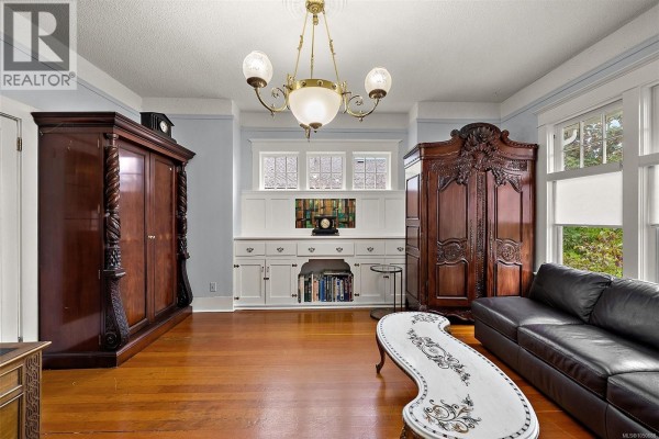 Living room with two large wooden armoires, a black leather sofa, and built-in shelving. - 1528 Foul Bay Rd, Victoria