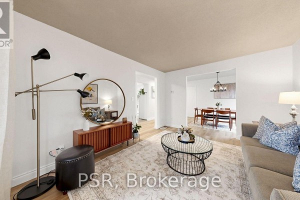 Living room with a sofa, coffee table, and view into a dining room with a chandelier. - 1528 Wildlark Drive, Peterborough