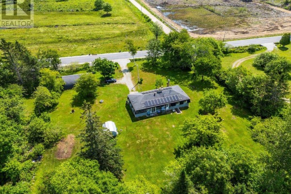 Aerial view of a grey house with solar panels, set in a grassy lot with trees and a road. - 153 Argyle Head Road, Argyle Head