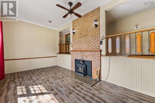 Living room with a brick fireplace and wood-look flooring, featuring a ceiling fan and wall paneling. - 153 Argyle Head Road, Argyle Head