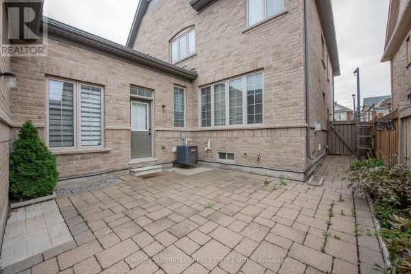 Backyard brick exterior with a patio, door, and pathway leading to a wooden fence. - 153 Barons Street, Vaughan
