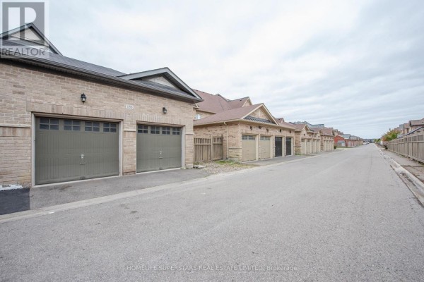 Rear view of a street with attached garages and brick townhouses on both sides. - 153 Barons Street, Vaughan
