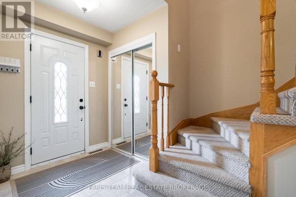 Interior foyer with a staircase, beige walls, mirrored closet doors, and tile flooring. - 153 Cardinal Street, Barrie