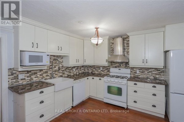 White kitchen with a farmhouse sink, granite countertops, and mosaic tile backsplash. - 153 Hale Street, London East