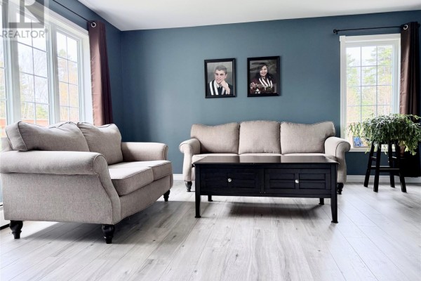 Living room with beige sofas, a dark coffee table, and windows overlooking a wooded area. - 153 Main Street, Lourdes