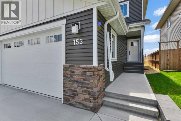 Close-up view of the house entrance featuring dark grey siding, stone accent pillar, white garage door, and glass-paned front door. - 153 Norseman Close, Penhold