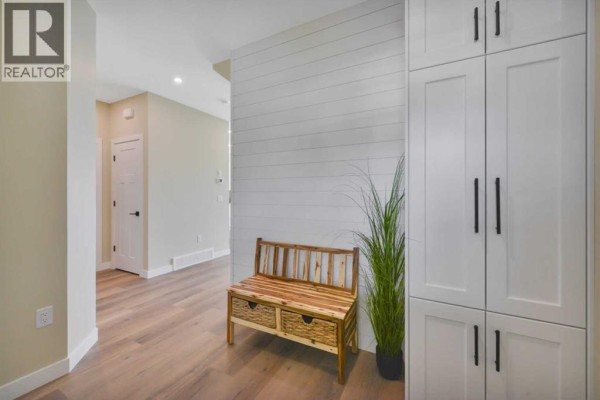 Entryway with light wood-look laminate flooring, a rustic wooden bench with woven storage baskets, and a tall white storage cabinet. - 153 Norseman Close, Penhold