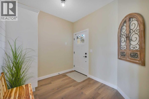 Entrance hall showing a white front door with glass panes, neutral walls, and a decorative wooden wall accent piece. - 153 Norseman Close, Penhold