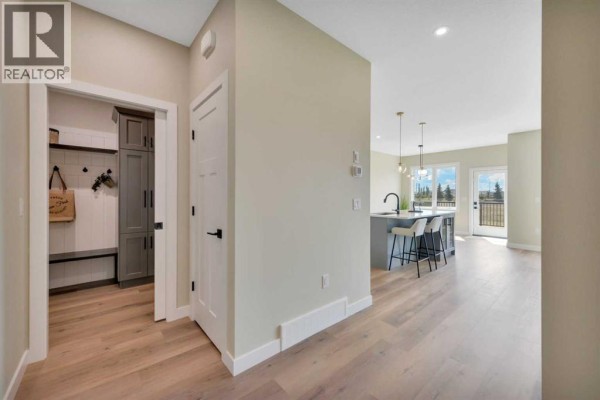 Hallway with light wood laminate floors leading to an open-concept kitchen and dining area with a large island and view of the backyard. - 153 Norseman Close, Penhold