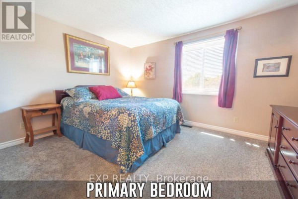 A primary bedroom with a bed, nightstand, and dresser against a beige wall. - 153 Oneida Place, Kitchener