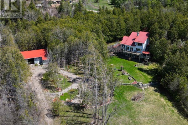 Aerial view of a house and barn nestled within a forested landscape with open grassy areas. - 153 Pleasant Point Road, Kawartha Lakes