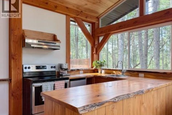 The kitchen includes a stainless steel stove, wood counters with a live edge, and large windows. - 221 Sockeye Dr, Mudge Island