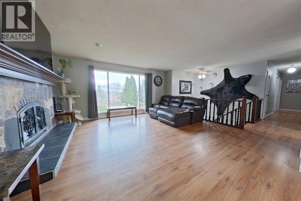 Living room with stone fireplace, large window, and hardwood flooring - 1530 21 Highway, Creston