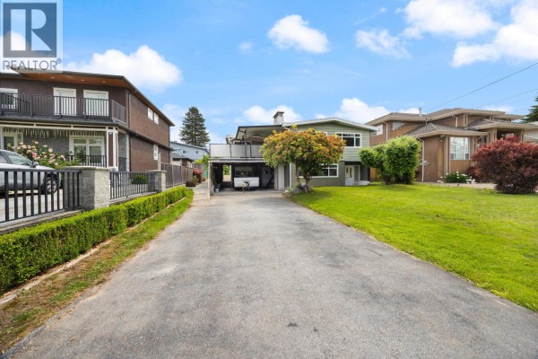 View of a paved driveway leading to a green house with a side yard and neighboring houses. - 1530 Sherlock Avenue, Burnaby
