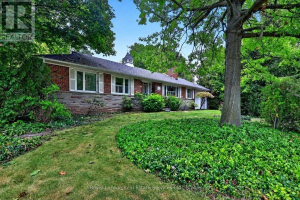 Side view of a brick bungalow with white shutters, situated on a large lot with dense foliage. - 1531 Duncan Road, Oakville