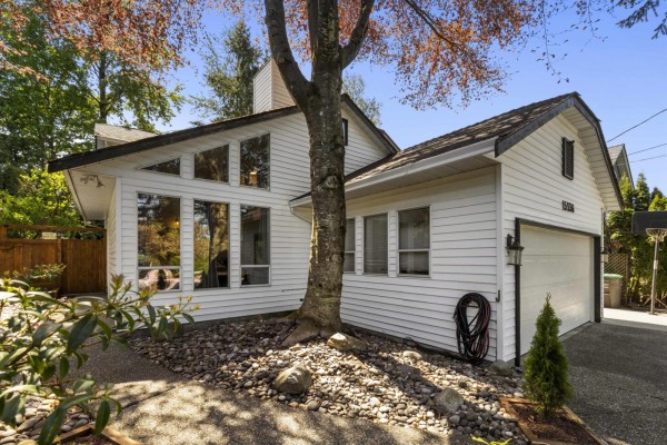 Close-up of the white house exterior with angled windows and a mature tree. - 15336 112 Avenue, Surrey