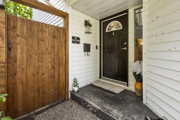 Front entrance of the house with a black door, wood gate, and concrete steps. - 15336 112 Avenue, Surrey