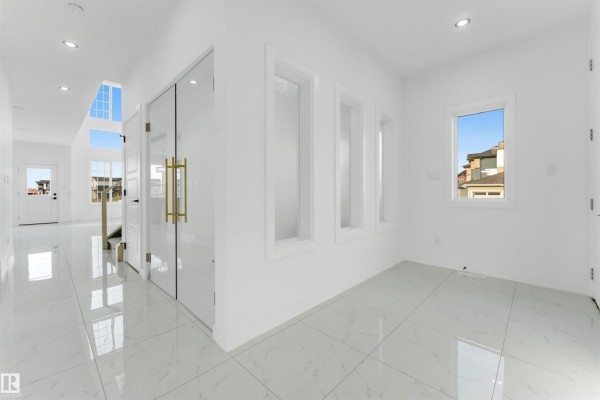 View of the living room with a tall fireplace, white tile floors, large windows, and a modern glass-railed staircase. - 1536 64 Ave Ne, Rural Leduc County