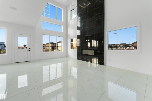 Open-concept living space featuring a large white marble island with gold hardware, multiple windows, and a tall black fireplace. - 1536 64 Ave Ne, Rural Leduc County