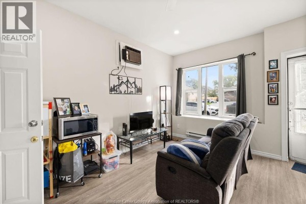 Living room with a grey sofa, television, microwave, and a large window overlooking the street. - 1537 Howard, Windsor