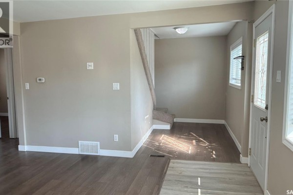 Living room with beige sofa, ottoman, and doorway to bedroom on left. - 1537 Second Street, Estevan