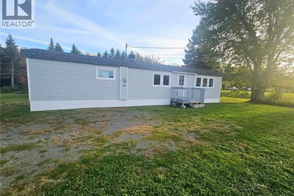 Side exterior of a light blue vinyl-sided single-wide mobile home showing the deck and surrounding lawn. - 1539 Cormier, Robertville