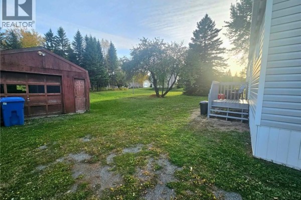 Backyard view of the mobile home deck, a shed with a garage door, and lawn area. - 1539 Cormier, Robertville