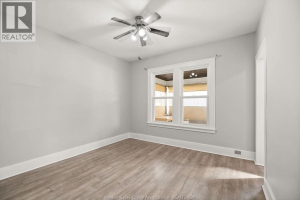 Empty room with light gray walls, white trim, wood-look laminate flooring, and ceiling fan. - 1539 Howard, Windsor