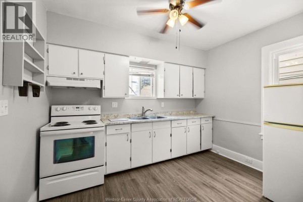 White kitchen with a white stove, double sink, and white cabinetry against gray walls. - 1539 Howard, Windsor