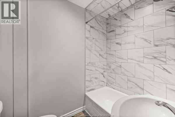 Bathroom with a white bathtub, white sink, and walls tiled with gray and white marble-look tiles. - 1539 Howard, Windsor