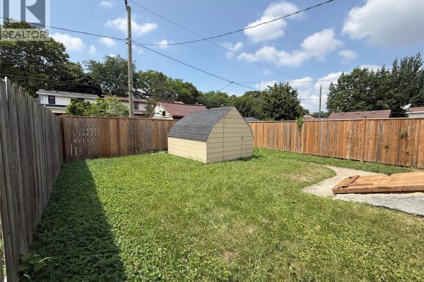 Backyard with a wooden fence, grass, a small yellow shed, and a concrete patio. - 1539 Windermere Road, Windsor